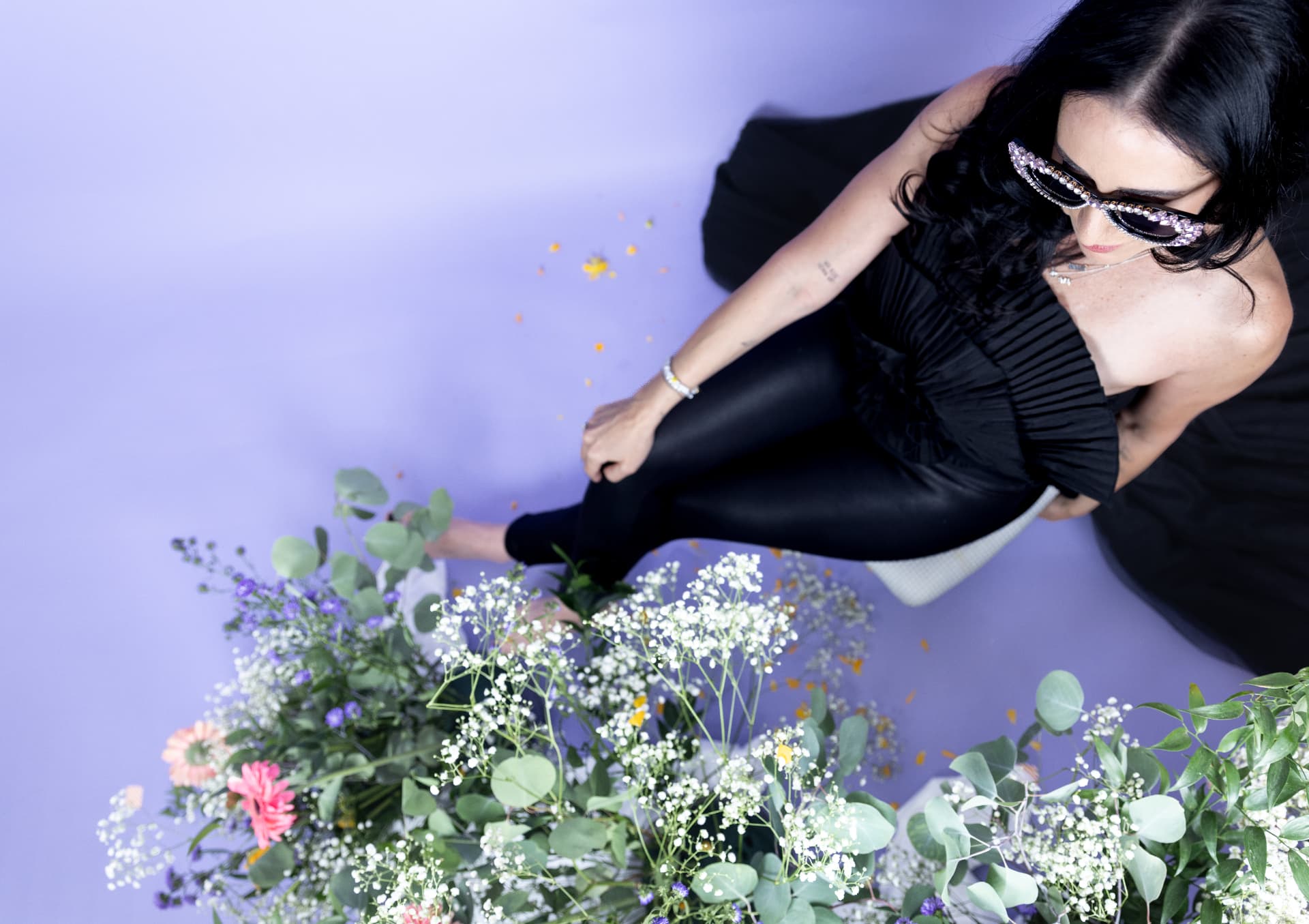 Rachel Sobel wearing jeweled sunglasses and a black ruffled dress against a purple backdrop